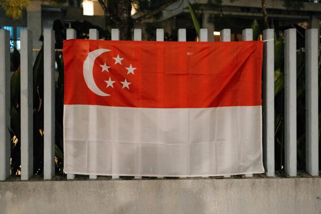 pexels-photo-31555750-31555750 The Singapore flag displayed outdoors on a metal fence during the night.